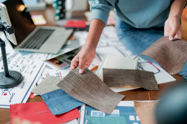 African american adult female woman fashion designer cloth tailor creative working for new collection sketch drawing measuring dress blouse choosing new color swatch fabric sample at her desk in her design studio home studio workshop
