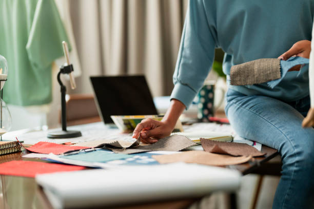 hand working close up of asia female fashion designer's hand design sketch and choosing sample of fabric swatch and textile for her new collection for new show in home studio office