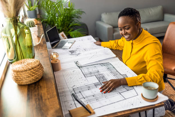 A shot of a young business woman looking at the camera while working with blueprints in the office