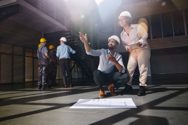 Real estate developers cooperating while making plans at construction building. Manual workers are in the background.
