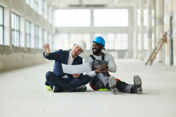 Happy project manager and black worker making plans while relaxing on floor at construction site. Copy space.
