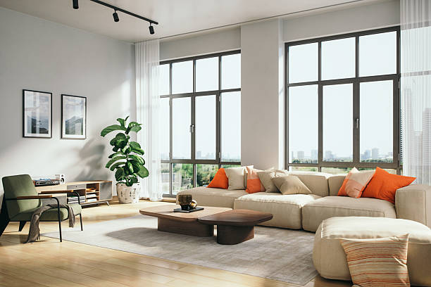 Spacious living room featuring a white sectional sofa with orange accent pillows, a low wooden coffee table, and floor-to-ceiling windows with sheer curtains.