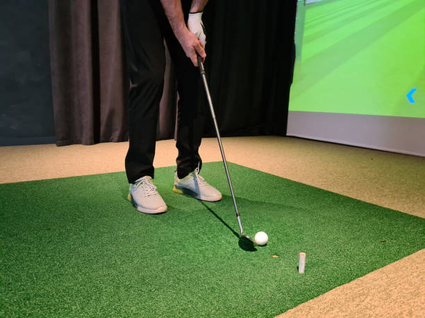 Golf player playing golf indoors on golf simulator closeup. Driving range with screen for golf and golfer legs